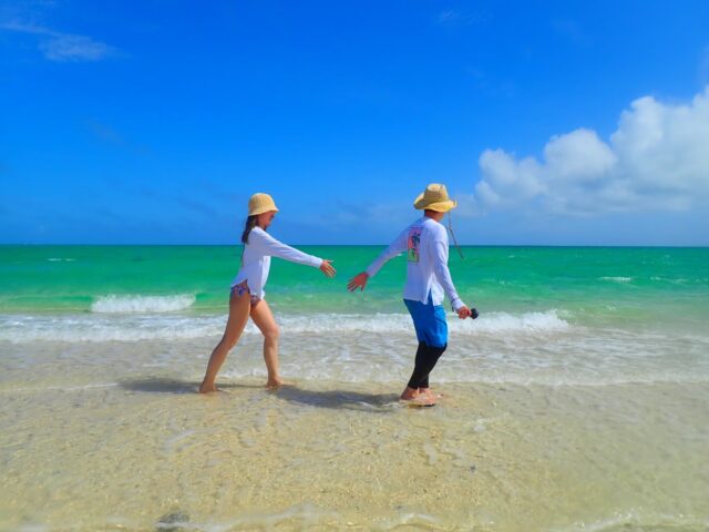 浅瀬を歩く帽子を被った男女のカップル。
